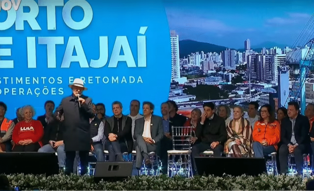 Presidente Lula, com uma roupa preta, discursando na cerimônia de retomada das operações do Porto de Itajaí, em Santa Catarina. Na imagem, podemos identificar Fernando Haddad e os irmãos Batista, da JBS.