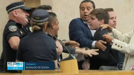 Na imagem está uma imagem de transmissão do SP2, pela TV Globo, que mostra o presidente do Sindimoto-SP, Gilberto Almeida dos Santos, e o vereador Lucas Pavanato (PL) em troca de empurrões em audiência na Câmara Municipal de SP, com a intervenção dos seguranças.