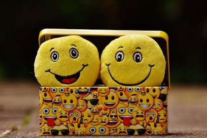 Two yellow smiley plush toys in an emoji-themed box, expressing fun and happiness.