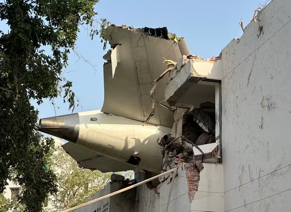 A cauda do avião Boeing 787 Dreamliner da Air India que caiu é vista presa a um prédio após o acidente - Foto: Amit Dave/Reuters